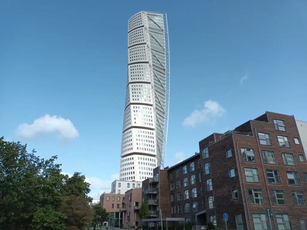 [:en]Turning Torso in Malmö. A tall white building that twists around its axis. Lower dark buildings next to each other.[:]