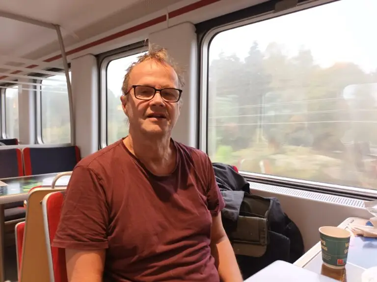 [:en]The man is sitting in the train's dining car.[:]