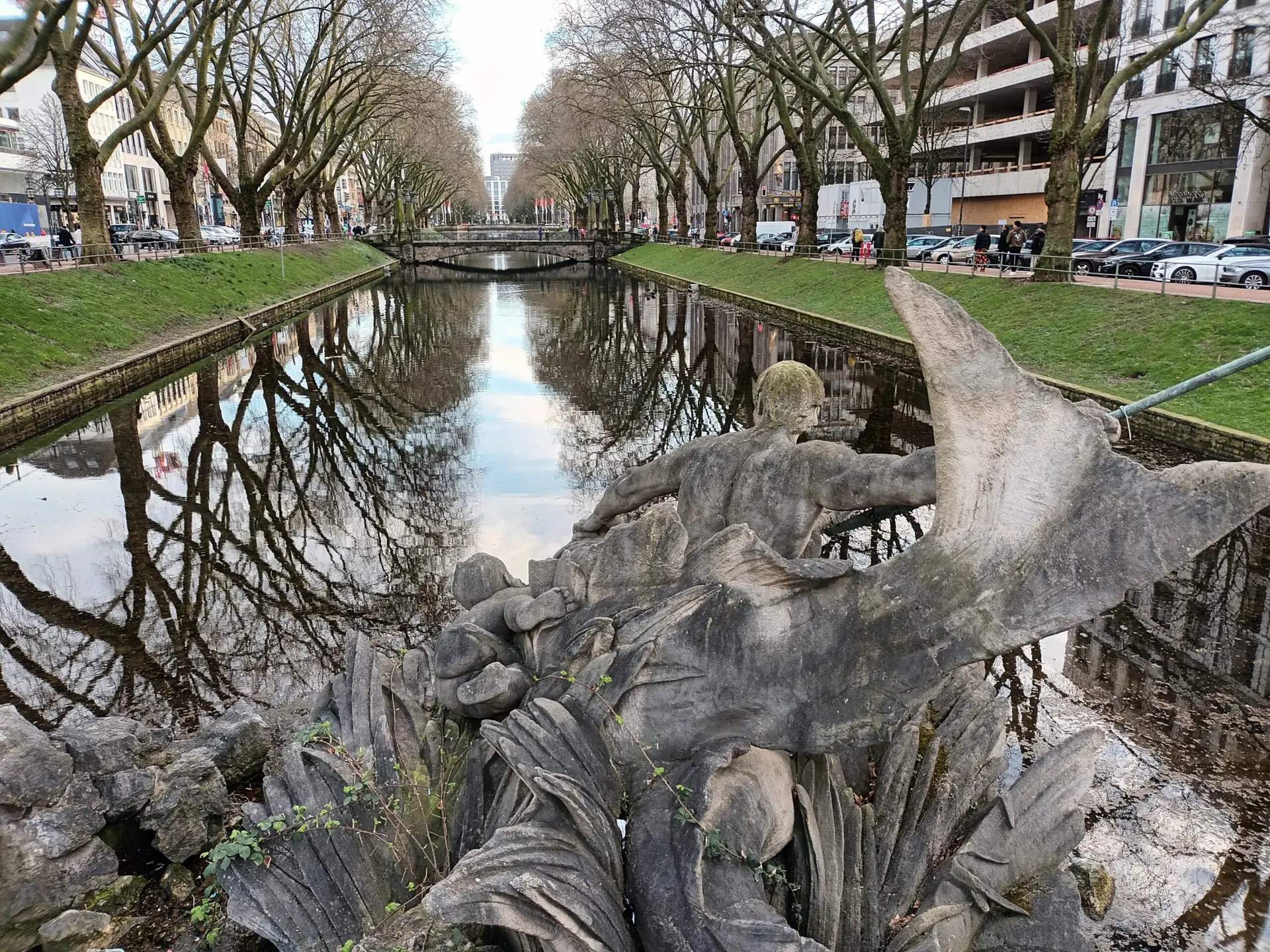 [:en]The trees on Düsseldorf's Königsallee are beautifully reflected in the surface of the water of the river between the streets.[:]
