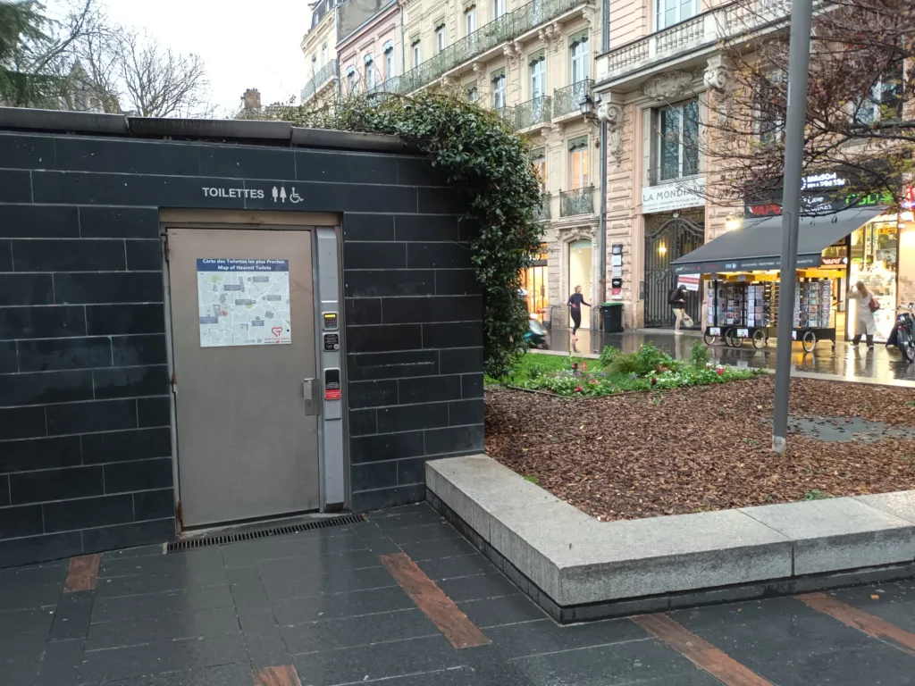 [:en]Free toilet in Toulouse. The wall and door of the toilet. Next to it, the wall of a big house is visible.[:]