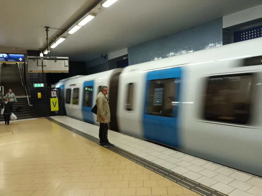 [:en]A man is standing on the platform and a subway train rushes by.[:]