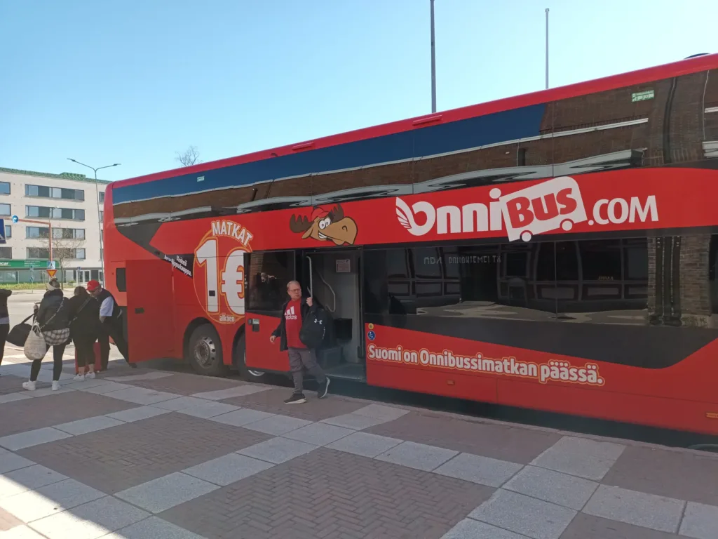 [:en]Passenger exiting the bus at the bus station. Other passengers are waiting for their luggage from the hold.[:]