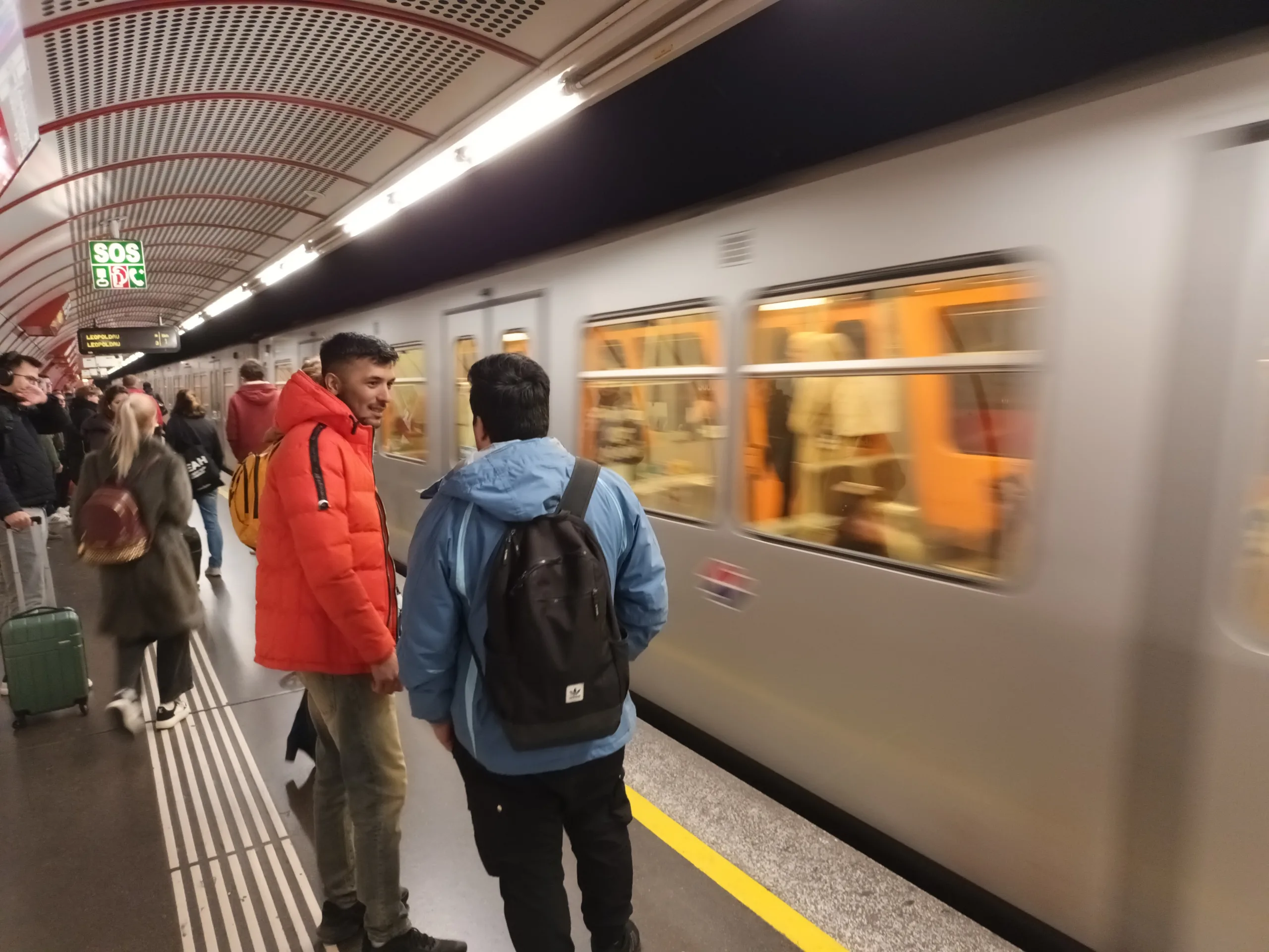[:en]The subway train arrives at the station in the Vienna underground. People are chatting on the platform.[:]